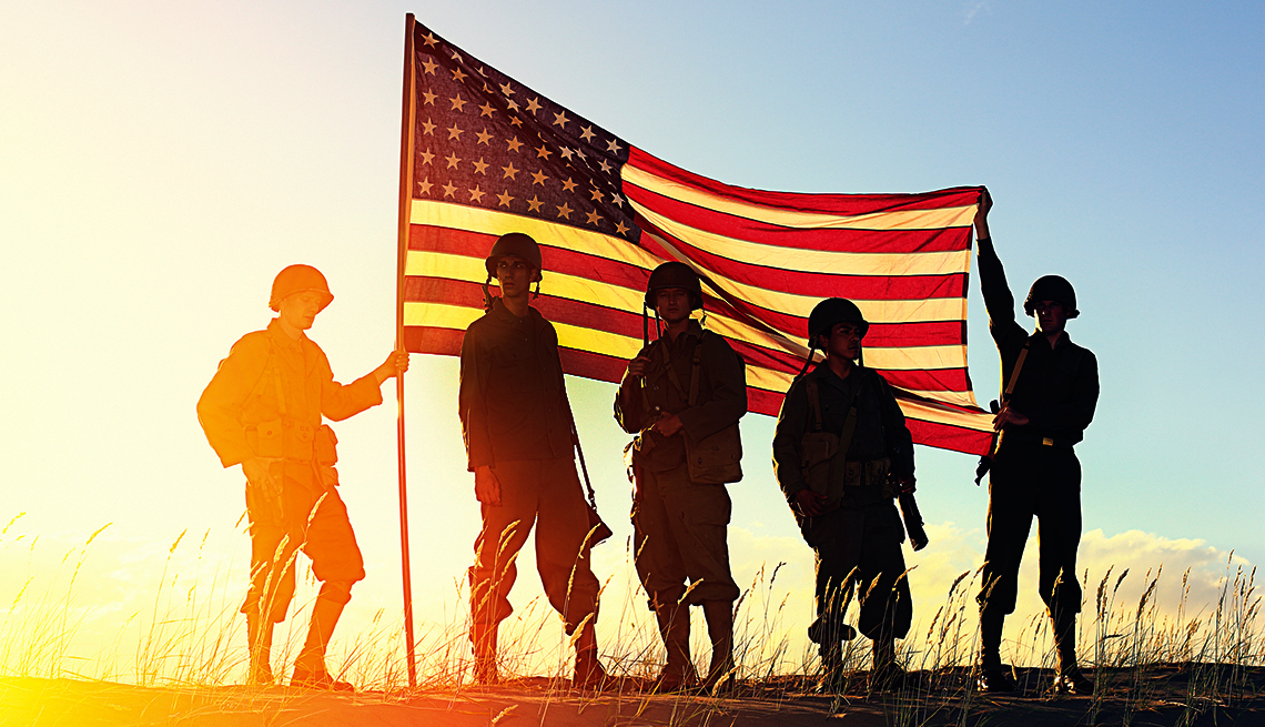 Silhouettes of American service members holding the U.S. flag at sunset